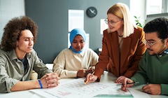 Four people sit around a table in discussion, looking at papers.